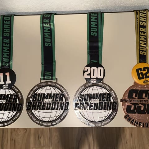 Geoff and Jenn’s Summer Shredding 2026 medals and competitor badges laid out together