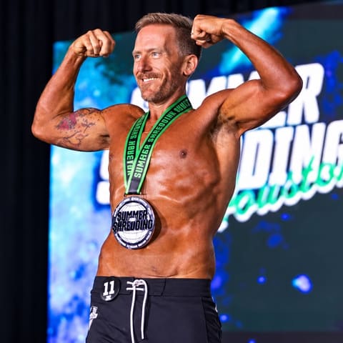Geoff flexing on stage at Summer Shredding Houston with his medal